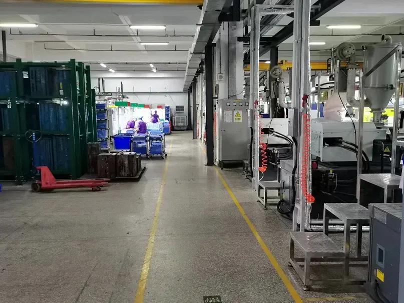 A marked aisle between molding machines and material racks at Xinyinhai, with employees in the distance