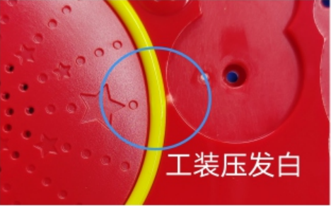 A blue circle marks whitening beside a yellow curved strip on a red assembly, attributed to fixture pressure.